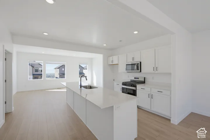Open-concept kitchen featuring white cabinetry, stainless steel appliances, a center island with sink, recessed lighting, and wood-finish flooring
