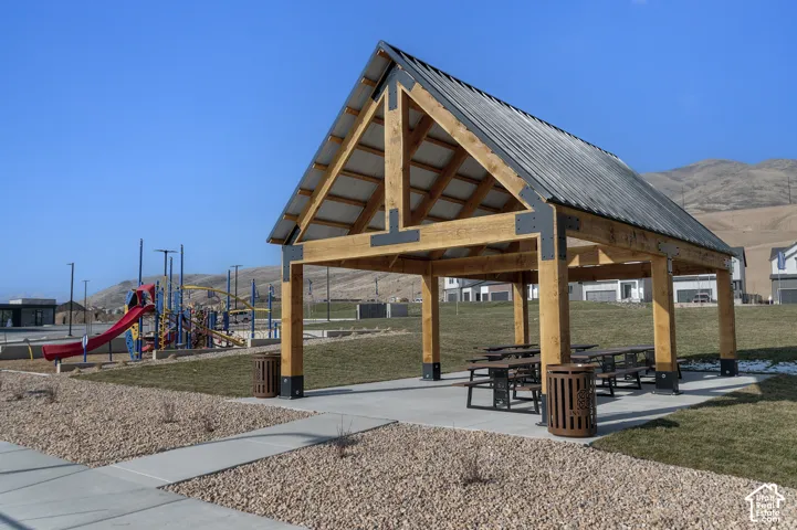 Timber frame pavilion with a corrugated metal roof, integrated picnic tables, and a playground area with a red slide