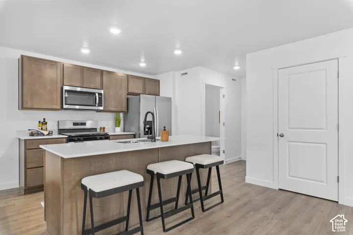 Kitchen featuring an island with white countertop, brown cabinetry, stainless steel appliances, and wood-finish flooring