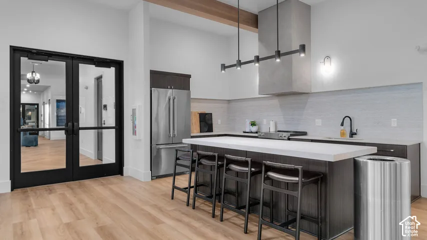 Spacious kitchen area featuring wood-finish flooring, a large island with seating, dark wood cabinetry, a contemporary range hood, and stainless steel appliances