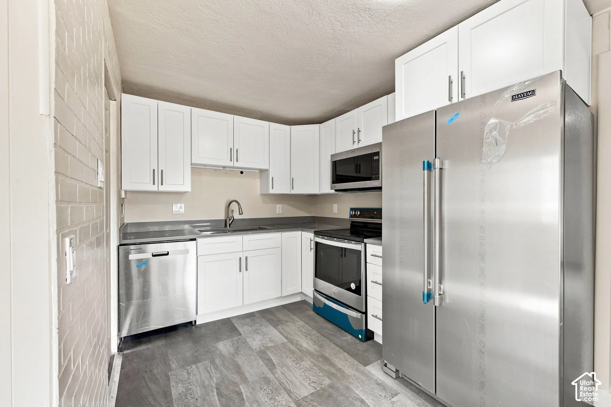 Kitchen featuring white cabinetry, stainless steel appliances, dark countertops, a gooseneck faucet, and wood-finish flooring