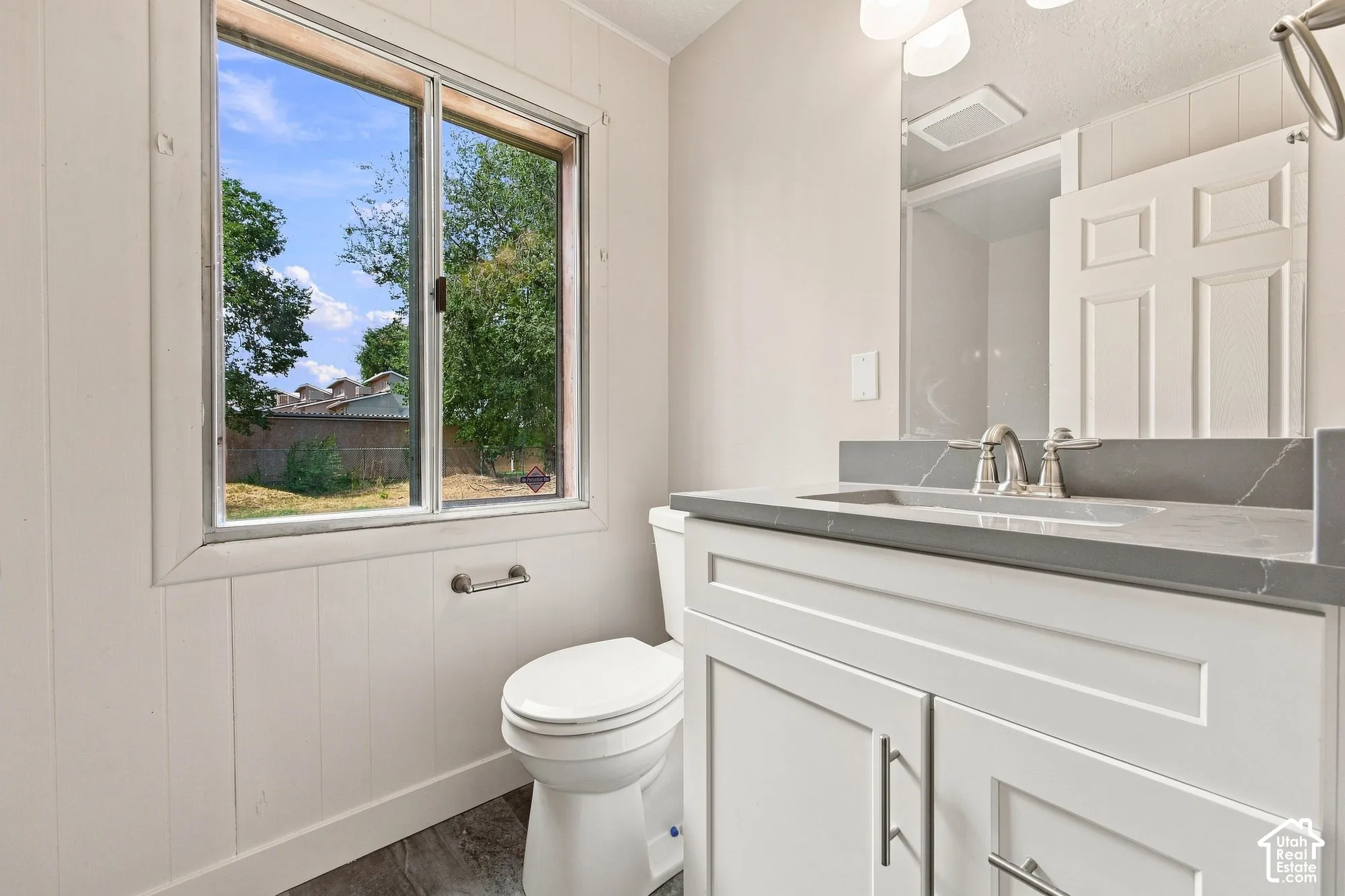 Bathroom featuring a white vanity with a gray countertop, an undermount sink, a dual-handle faucet, and vertical paneling on the walls