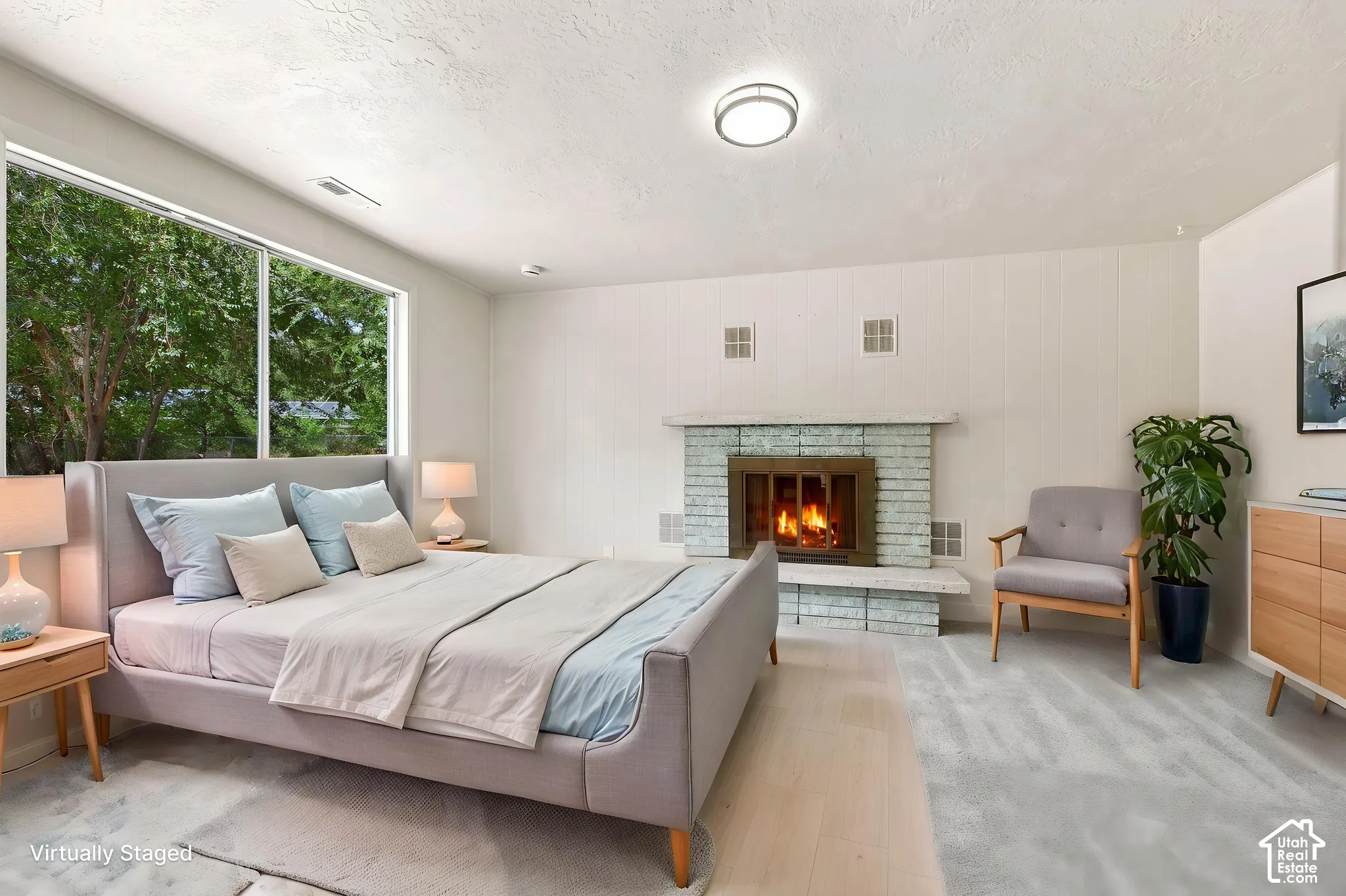 Large picture window with exterior greenery, masonry fireplace with a raised hearth, wood-finish flooring, and wall-to-wall carpeting