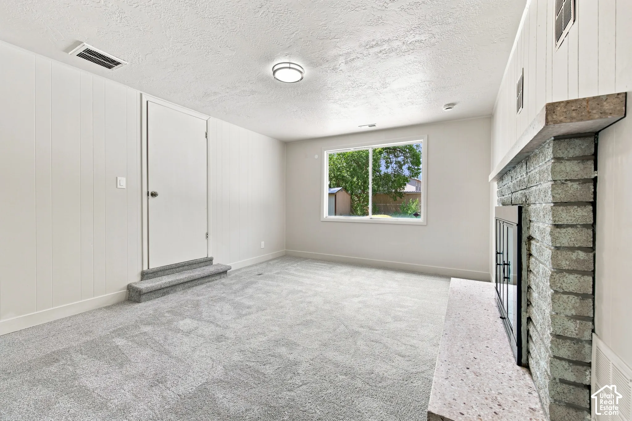 Recessed lighting, light gray carpeting, and a brick fireplace with a stone hearth