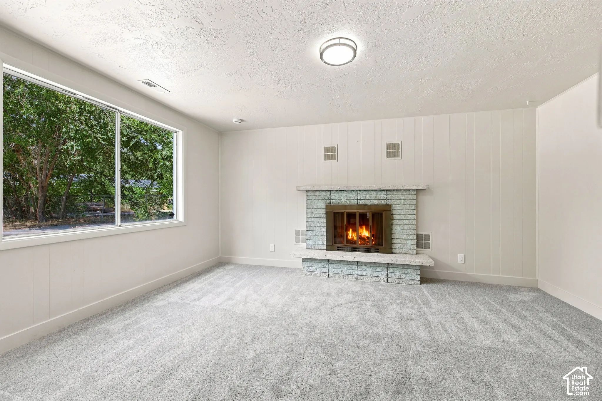 Expansive window, fireplace with a brick surround, and light gray carpeting