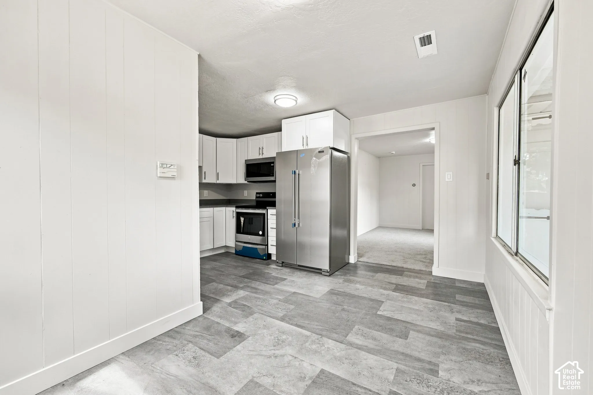 Kitchen featuring white cabinetry, stainless steel appliances, dark countertops, and wood-finish flooring