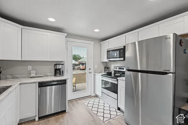 White shaker cabinetry, wood-finish flooring, stainless steel appliances, recessed lighting, and light-toned countertops