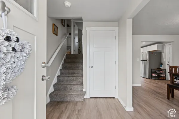 Wood-finish flooring, white trim, staircase with carpeted treads, white interior doors, and stainless steel refrigerator