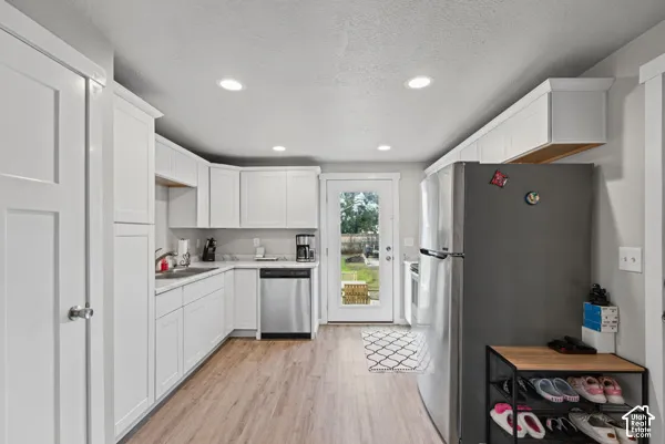 White shaker cabinetry, stainless steel dishwasher, wood-finish flooring, recessed lighting, and a glass-paneled exterior door