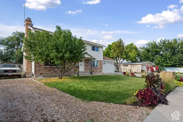 Brick and siding exterior with an attached garage, featuring a gravel driveway, mature trees, and landscaped garden beds