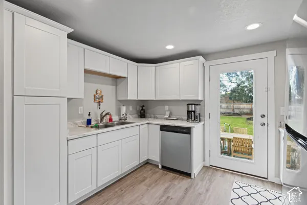 White shaker-style cabinetry with crown molding, light-toned countertops, stainless steel dishwasher, wood-finish flooring, and a glass-paneled door