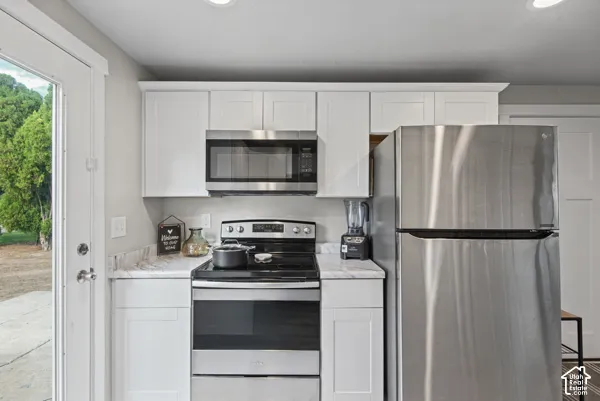 White shaker-style cabinetry, stainless steel appliances, marble-look countertops, and recessed lighting
