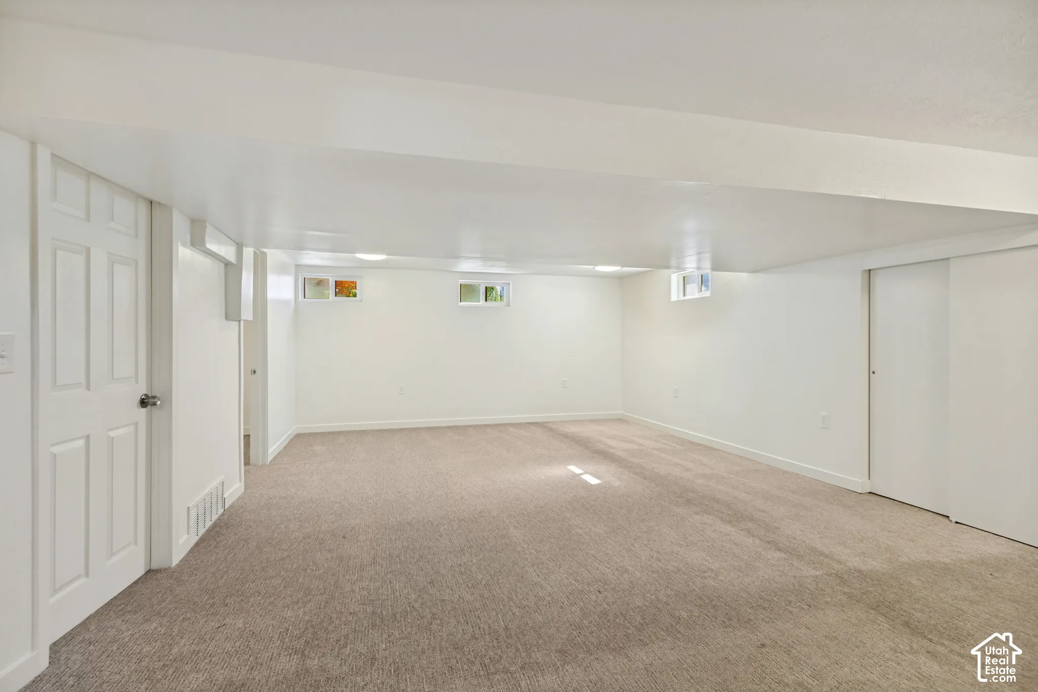 Expansive carpeted floor with white walls, multiple windows, and a white paneled door
