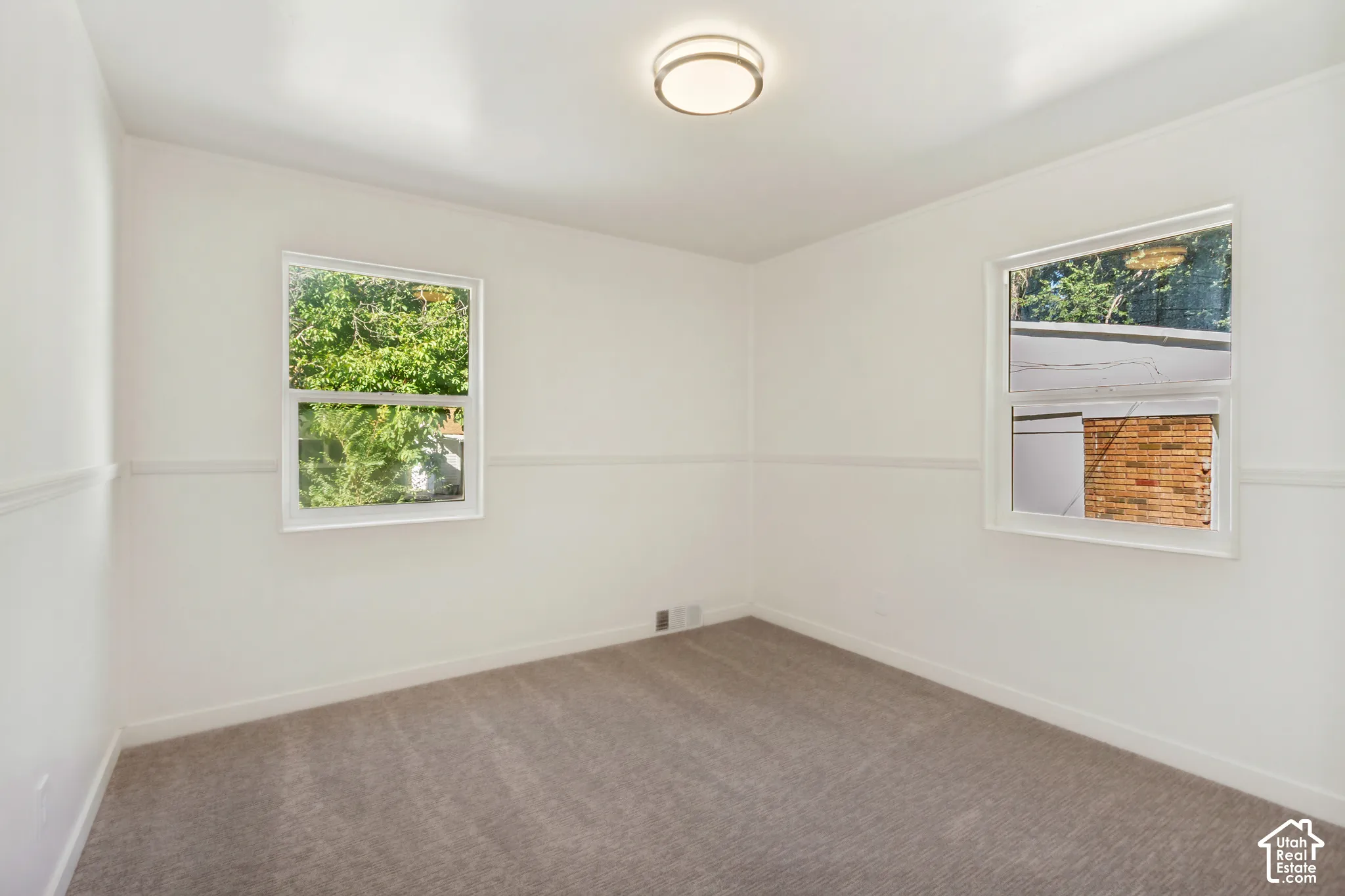 White walls with chair rail detailing, two windows, and a flush mount ceiling light