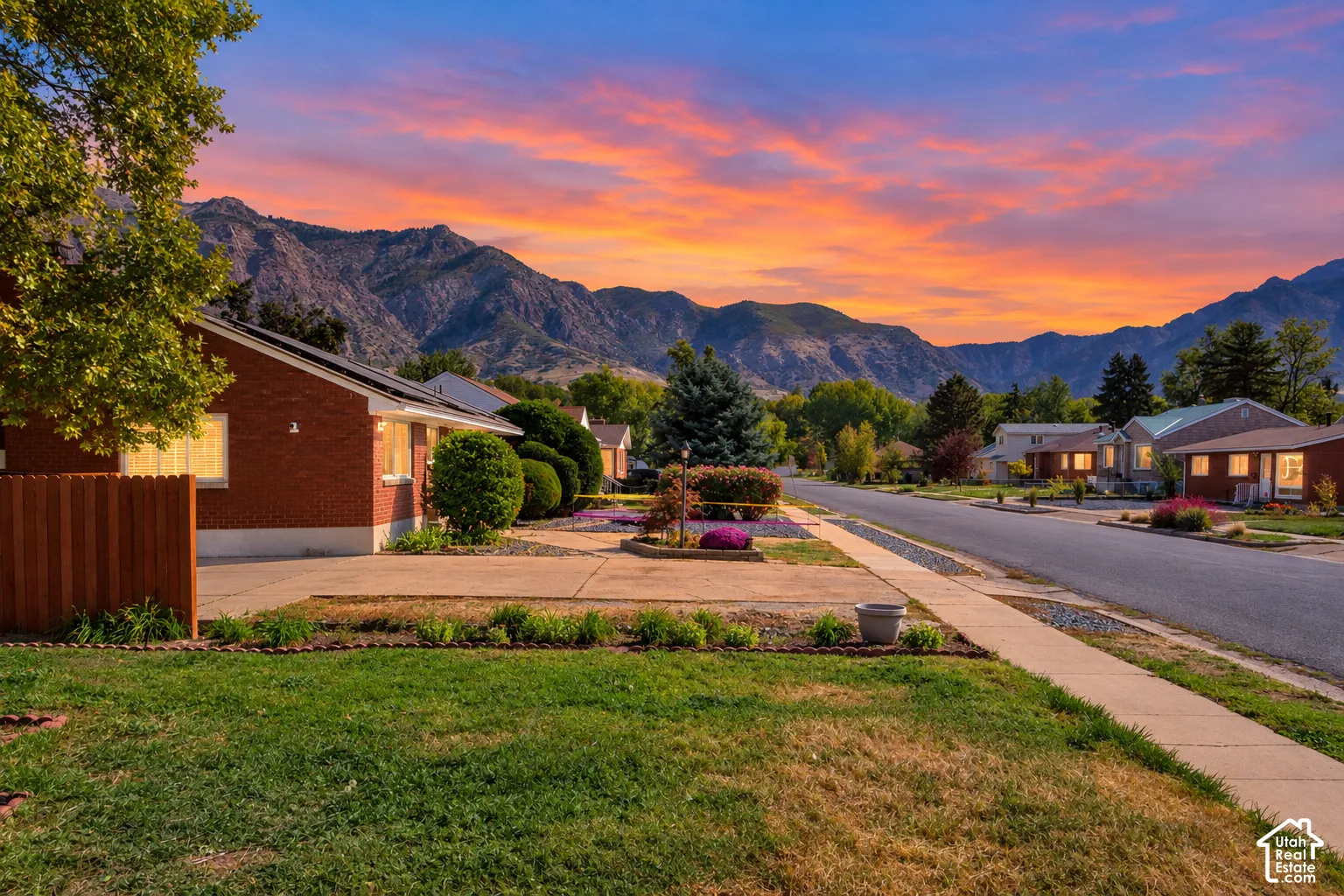 Brick exterior residence with solar panels, mature front yard landscaping, a concrete driveway, and a wood privacy fence