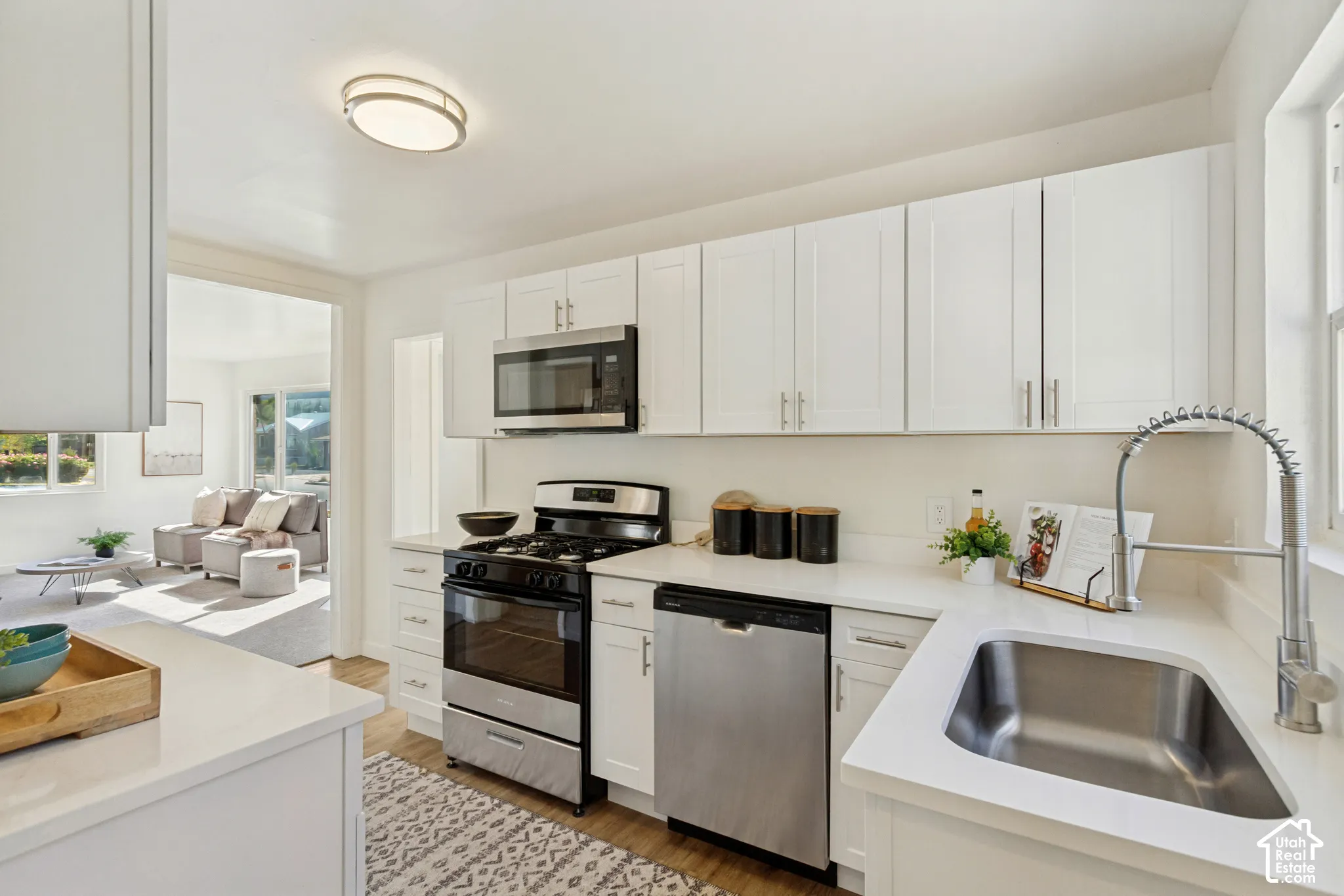 Modern kitchen featuring white cabinetry, light-toned countertops, stainless steel appliances, and wood-finish flooring
