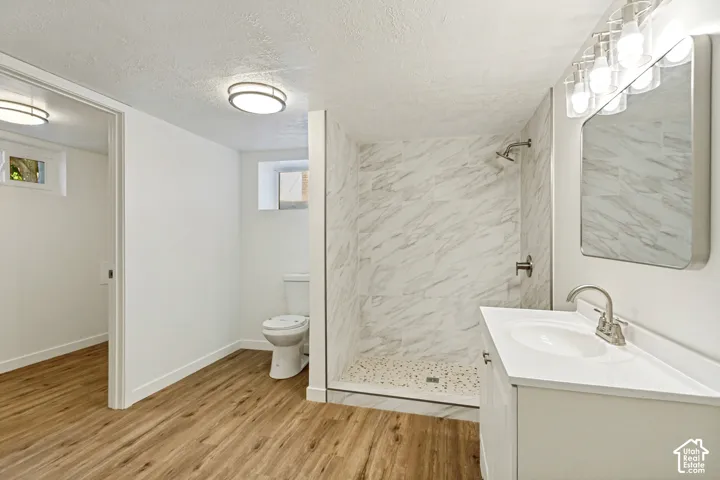 Wood-finish flooring, white vanity with integrated sink, chrome faucet, rectangular mirror, and a tiled shower with white and gray veining