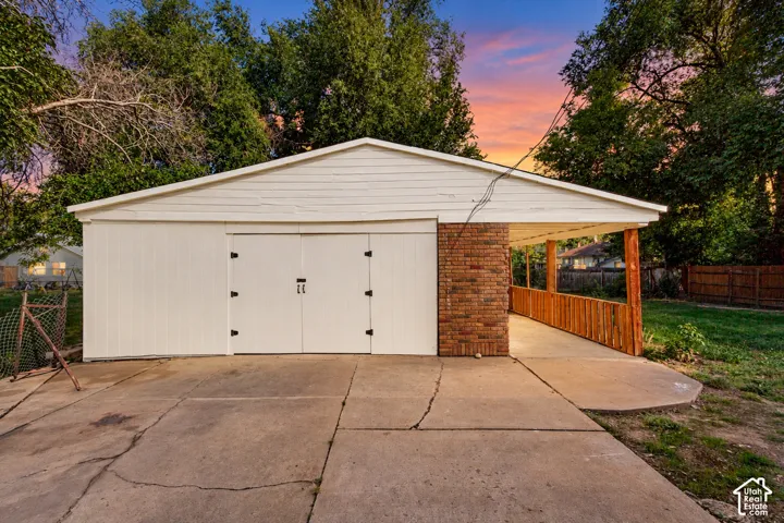 White exterior garage with double doors, featuring a brick-clad side wall and a covered walkway with a wooden railing