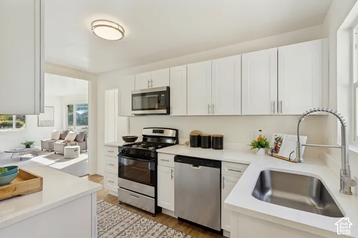 Modern kitchen featuring white cabinetry, light-toned countertops, stainless steel appliances, and wood-finish flooring