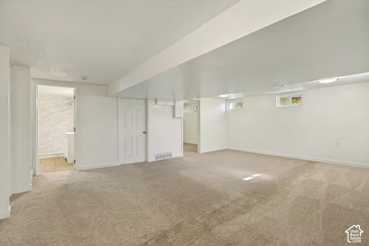 Expansive carpeted area with white painted walls, recessed lighting, and multiple windows