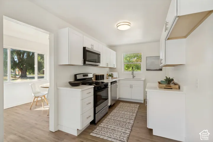 Modern kitchen featuring white shaker cabinetry, stainless steel appliances, light countertops, and wood-finish flooring