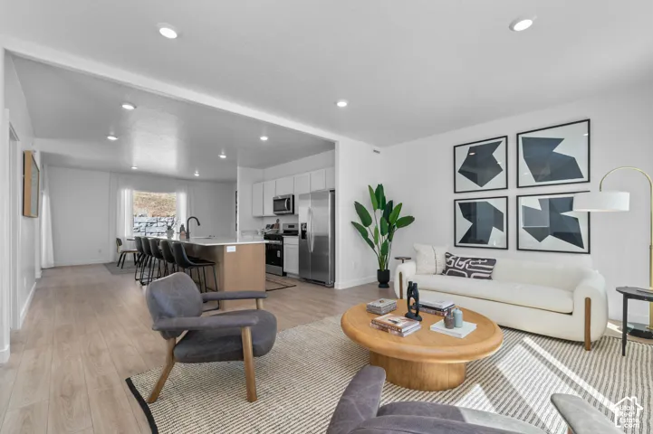 Recessed lighting, wood-finish flooring, white walls, kitchen island with seating, and stainless steel appliances