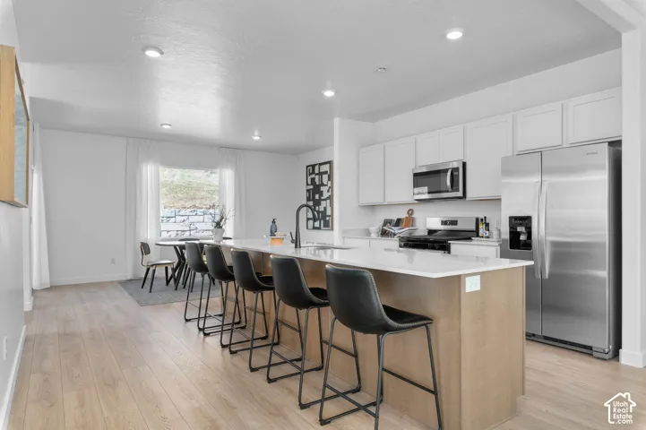 Open-concept kitchen with white shaker cabinetry, stainless steel appliances, and a central island with countertop seating
