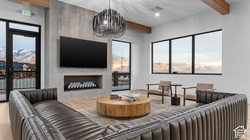 Modern fireplace with a mounted television, a linear chandelier, exposed wood ceiling beams, and large windows