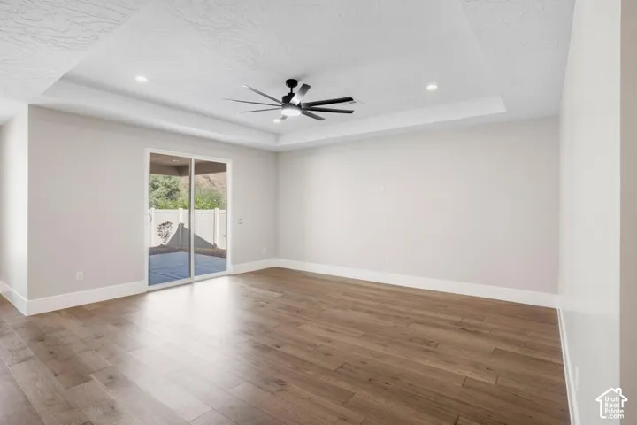 Wood-finish flooring, recessed lighting, ceiling fan, tray ceiling, and sliding glass door to exterior