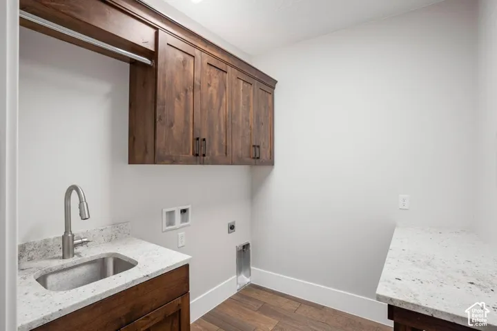 Wood-finish flooring, upper wood cabinetry, stainless steel sink, granite-style countertop, and a built-in hanging rod
