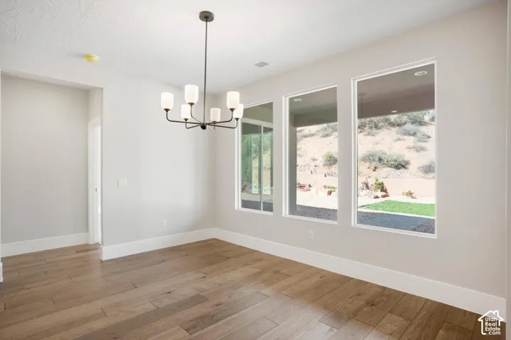 Spacious room featuring wood-finish flooring, white baseboards, and a contemporary chandelier