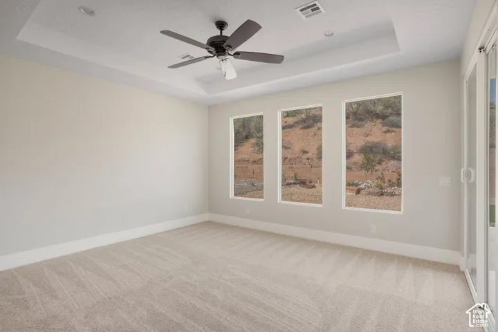 Tray ceiling with recessed lighting, ceiling fan, three vertical windows, sliding glass door, and neutral carpet