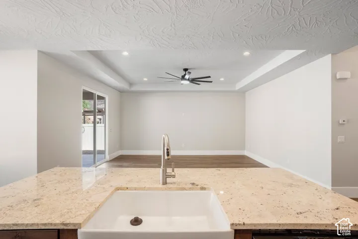 Granite-style countertop with farmhouse sink, brushed nickel faucet, wood-finish flooring, and recessed lighting with a ceiling fan