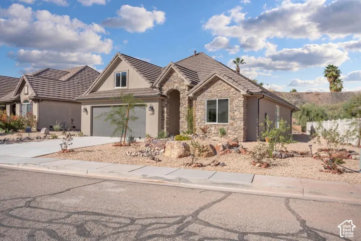 Exterior featuring stone and stucco finishes, a tiled roof, an arched entry, a two-car garage, and low-maintenance landscaping with decorative rock