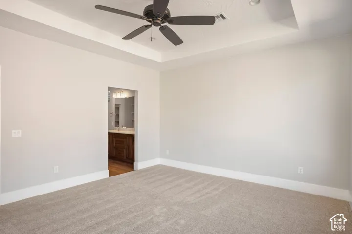 Tray ceiling with a ceiling fan, light neutral wall color, and carpeted flooring