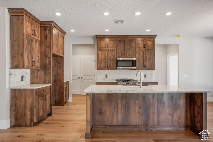 Wood-finish flooring, recessed lighting, wood cabinetry, stone countertops, and a kitchen island with a built-in sink