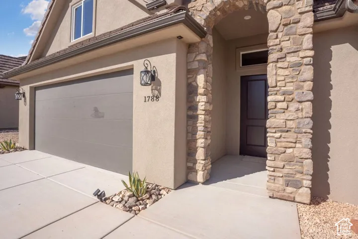 Stucco exterior with stone accents, a gray garage door, and a covered entry with an arched stone surround