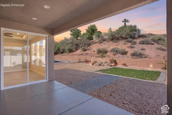Covered patio with concrete flooring opening to a landscaped backyard featuring drought-resistant plantings, mature trees, and rolling hillside backdrop