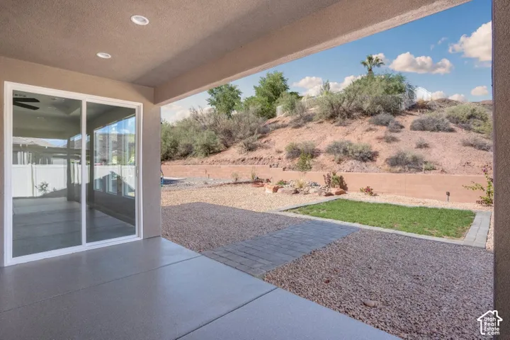 Covered patio with recessed lighting, large sliding glass door, paver stone walkway, gravel landscaping, and a small lawn area