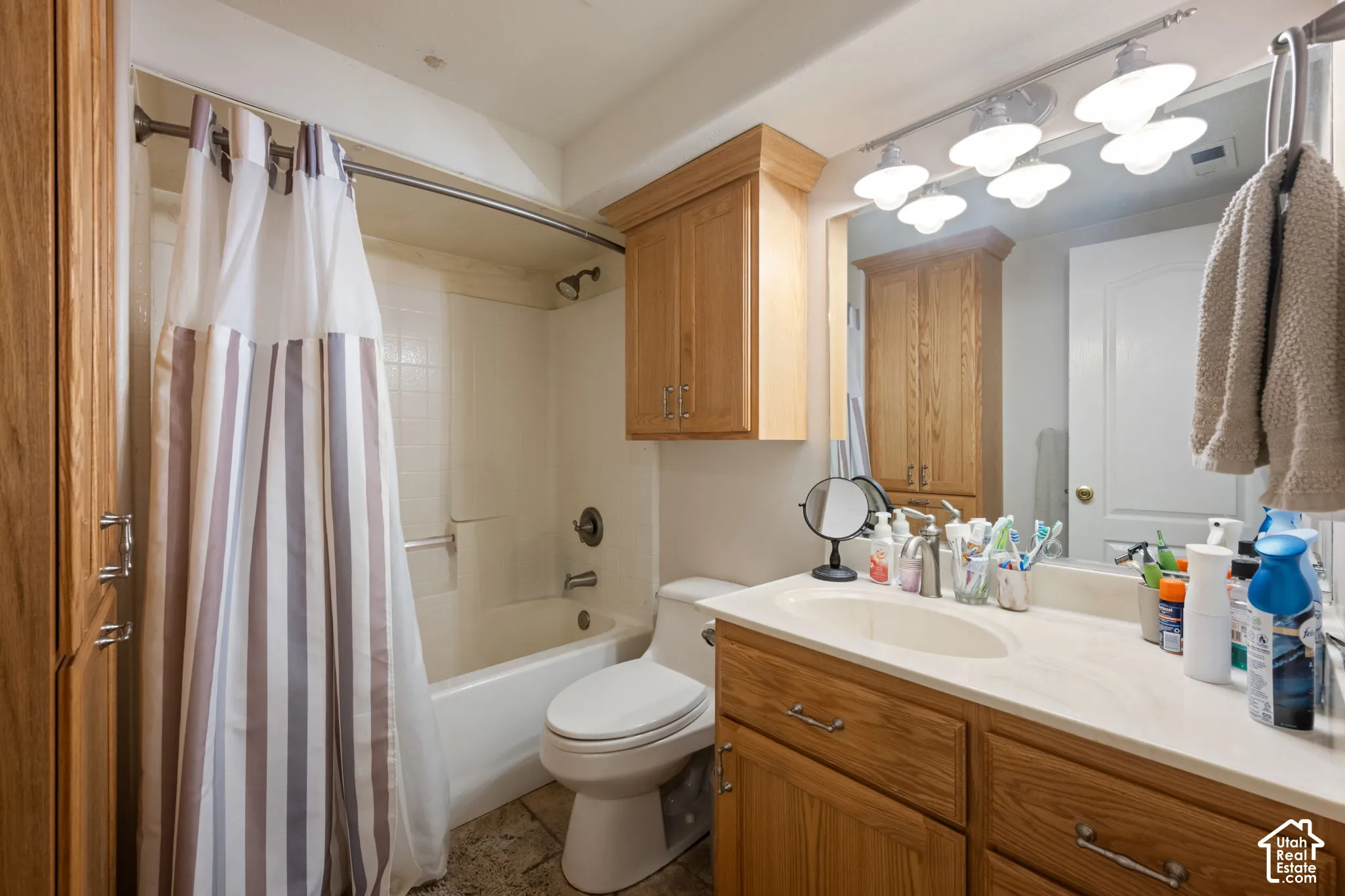 Bathroom featuring a single vanity with an integrated sink, wood-finish cabinetry, a built-in tub and shower combination, and tile flooring
