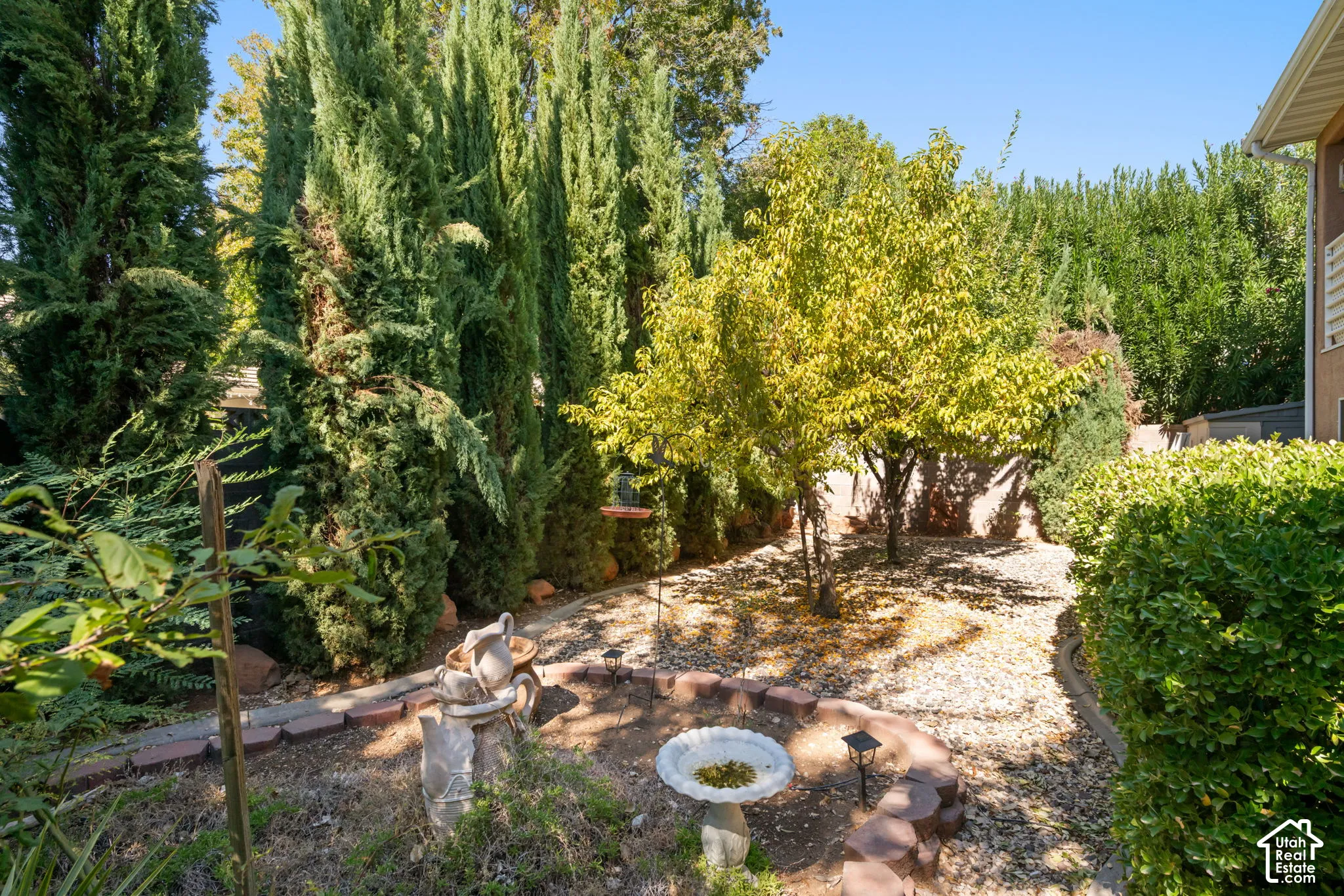 Landscaped exterior featuring tall evergreen trees, mature deciduous trees, a gravel ground cover, and a decorative bird bath