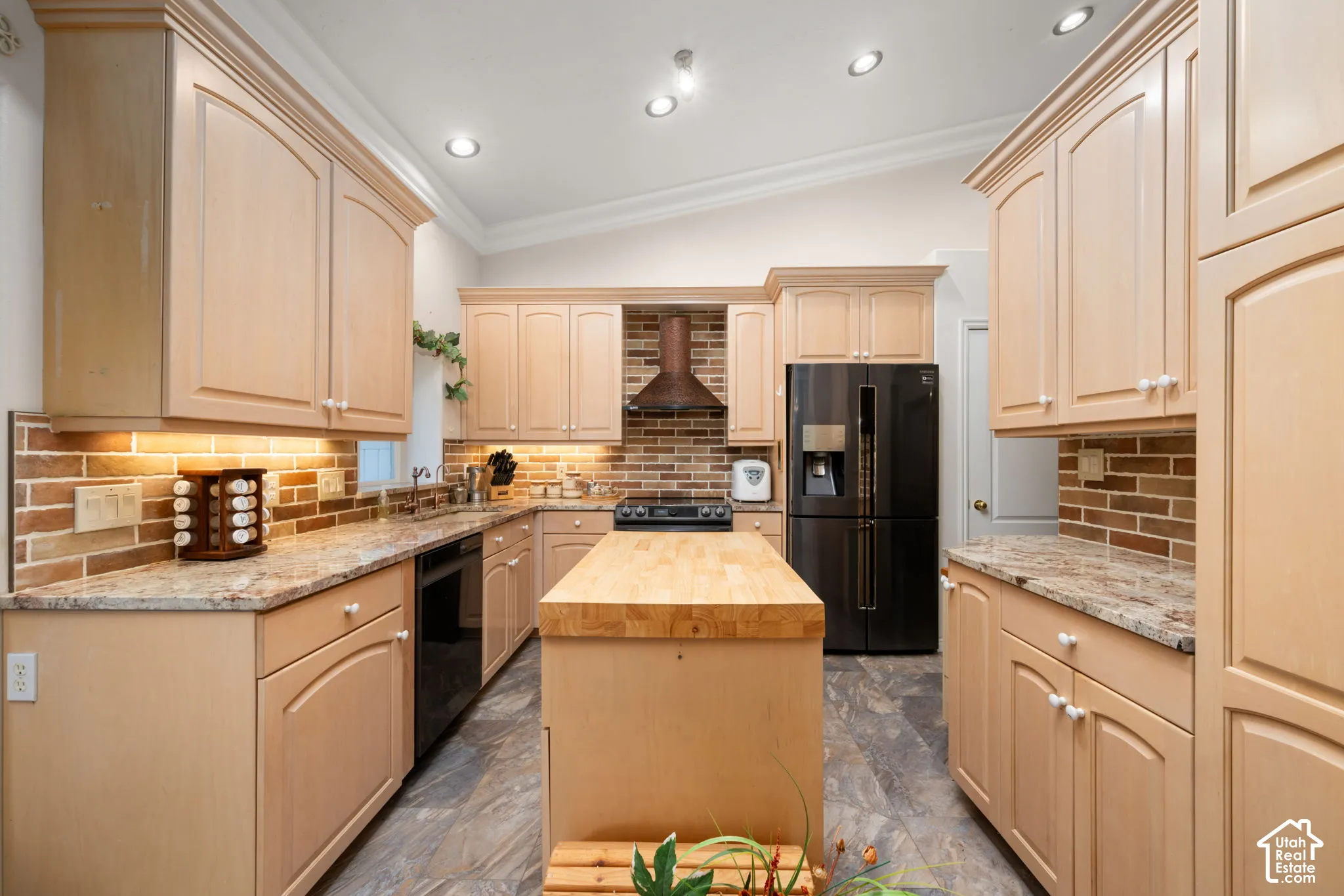 Kitchen with light wood-finish cabinetry, granite-style countertops, brick-style backsplash, and a central island with a wood butcher-block top