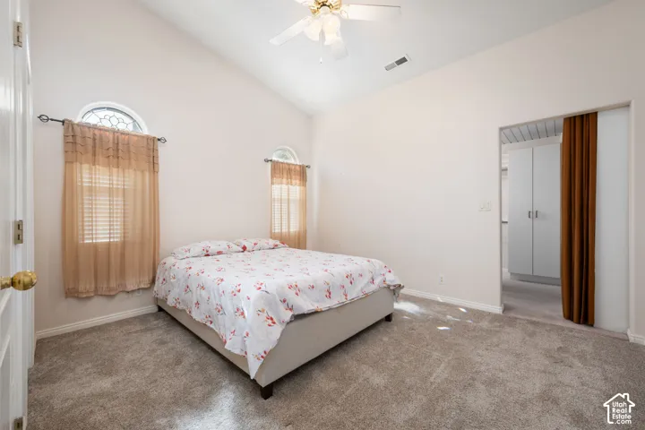 Vaulted ceiling with a ceiling fan, arched windows, and carpeted flooring