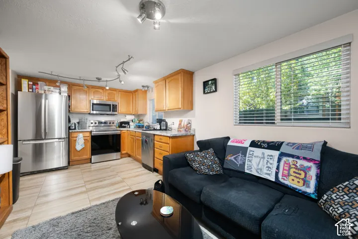 Kitchen with wood cabinetry, stainless steel appliances, and a tile floor, adjacent to a living area with a window