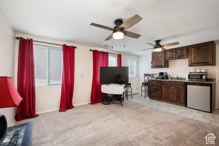 Open-concept living area featuring a compact kitchenette, two ceiling fans, and wood-finish cabinetry