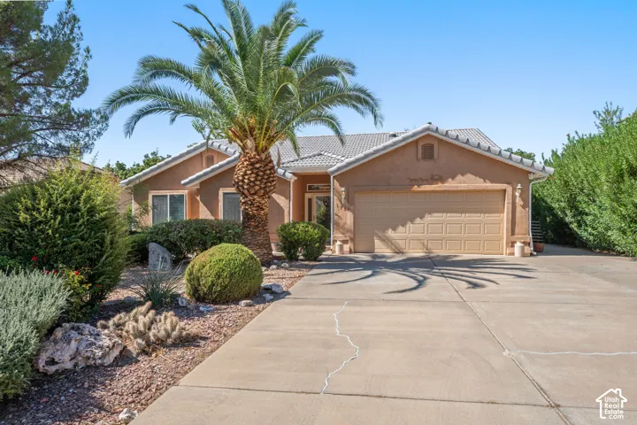 Stucco exterior with a tiled roof, desert landscaping, a palm tree, and an attached two-car garage