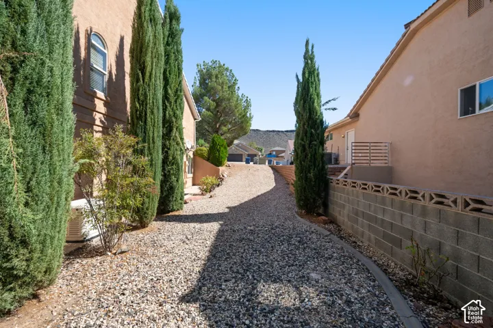 Gravel pathway bordered by established evergreen trees and a decorative block retaining wall