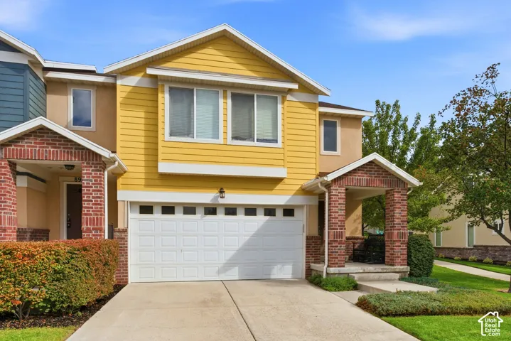 Residential exterior featuring yellow siding, brick accents, a two-car garage, concrete driveway, and a covered entry