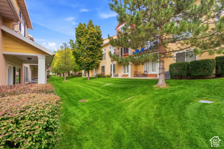 Expansive green lawn with mature trees and established shrubbery, complementing stucco exterior buildings featuring private patios and balconies