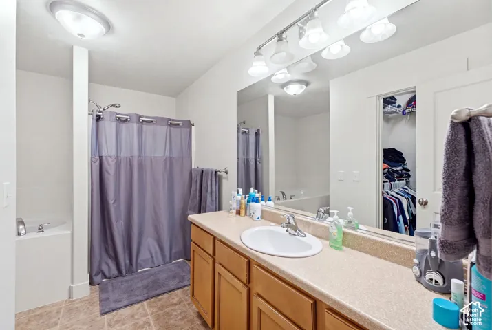 Bathroom featuring a single vanity with a laminate countertop, built-in tub, and tiled flooring